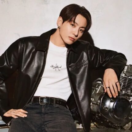Jungkook wearing a black leather racer jacket while posing beside a motorcycle.