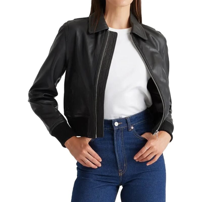 Woman wearing a black cropped leather bomber jacket open over a white top with blue jeans.