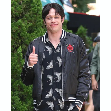Model wearing a black satin Okinawa bomber jacket with a red oni mask chest graphic, striped trims, and white sleeve stitching.