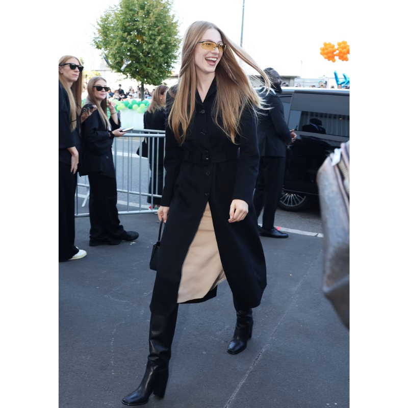 Untitled design (16) Hunter Schafer wearing the Hunter Schafer Black Coat, a long black coat with a button front, notched lapel collar, defined waist, and full-length sleeves.