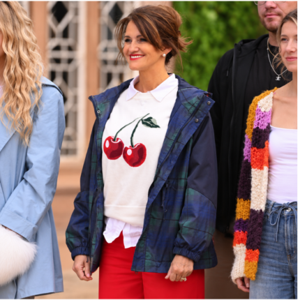 Woman wearing a navy blue and green hooded plaid jacket with a white cherry-print sweatshirt and red trousers.