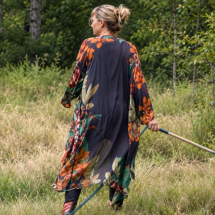 Model wearing a long navy floral kimono gown outdoors, showing the colorful back print and flowing silhouette.