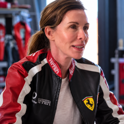 Carole Radziwill wearing a black Ferrari racing jacket with red and white panels and embroidered logo details.