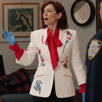Actress portraying Elsbeth wearing an ivory embroidered blazer with colorful floral designs, red ruffle cuffs, and a red neck bow.