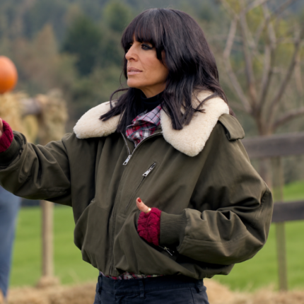 Claudia Winkleman wearing an olive green jacket with a cream sherpa fur collar, front zipper, and relaxed fit in The Celebrity Traitors Season 2.
