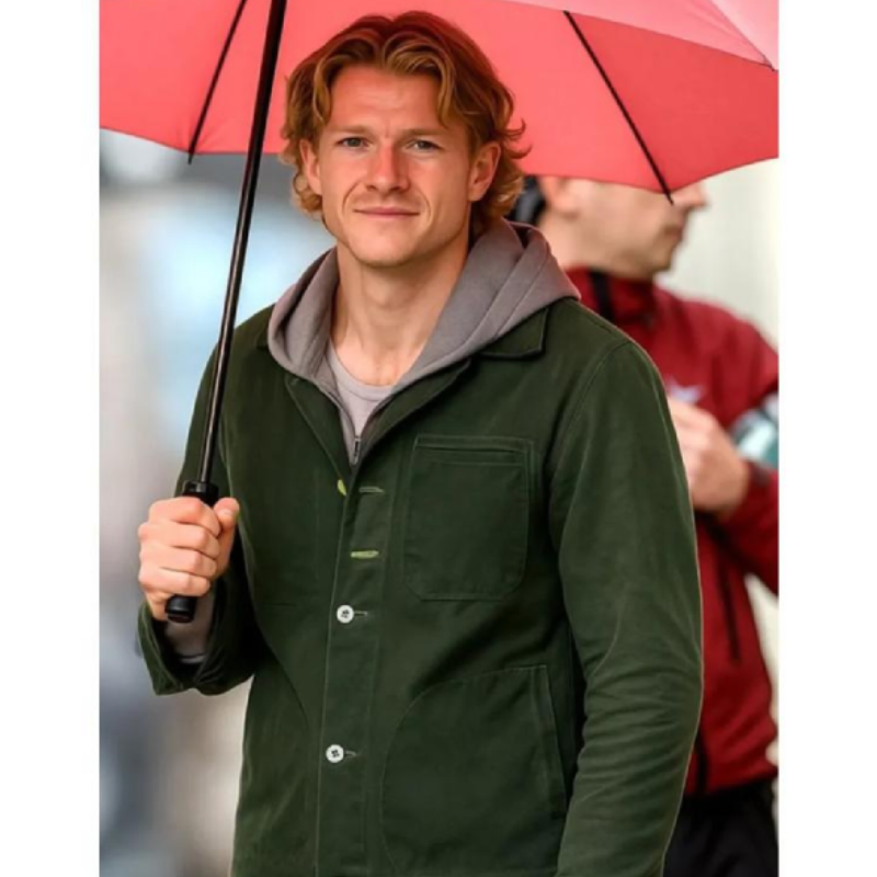 Clayface-2026-Matt-Hagen-Green-Jacket Tom Rhys Harries wearing a green Matt Hagen jacket with a chest pocket and button closure under a red umbrella.