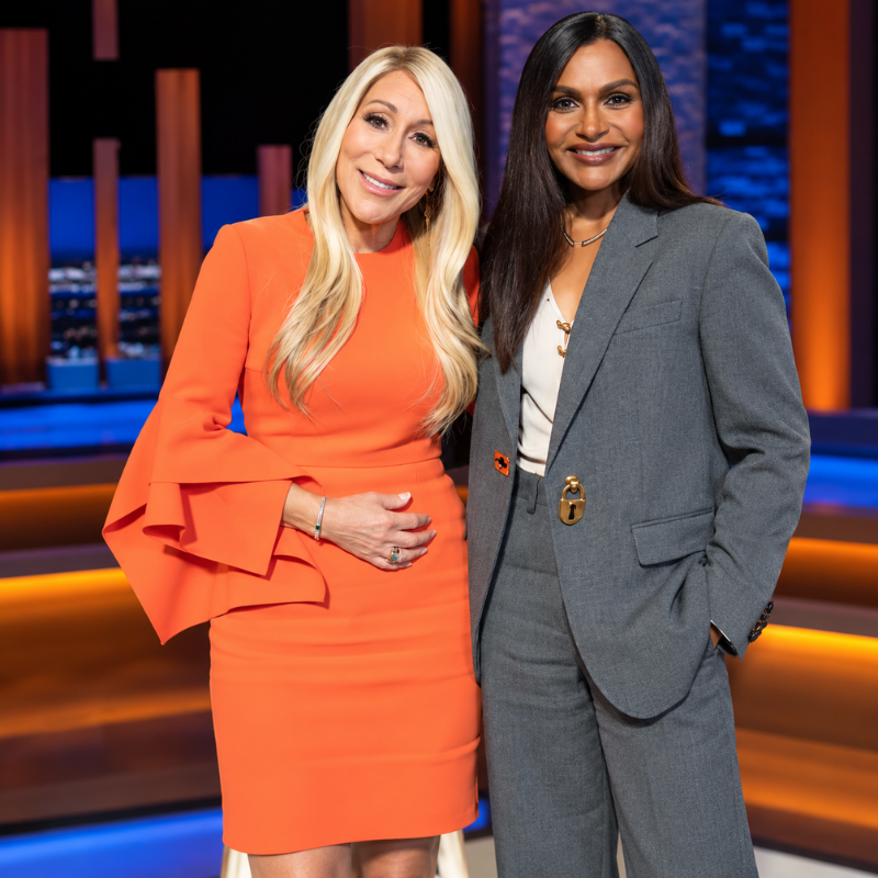 Greiner-shark-tank-season-18-roksanda-ruffled-midi-dress Woman wearing an orange fitted dress with layered bell sleeves and a round neckline on a studio-style television set.
