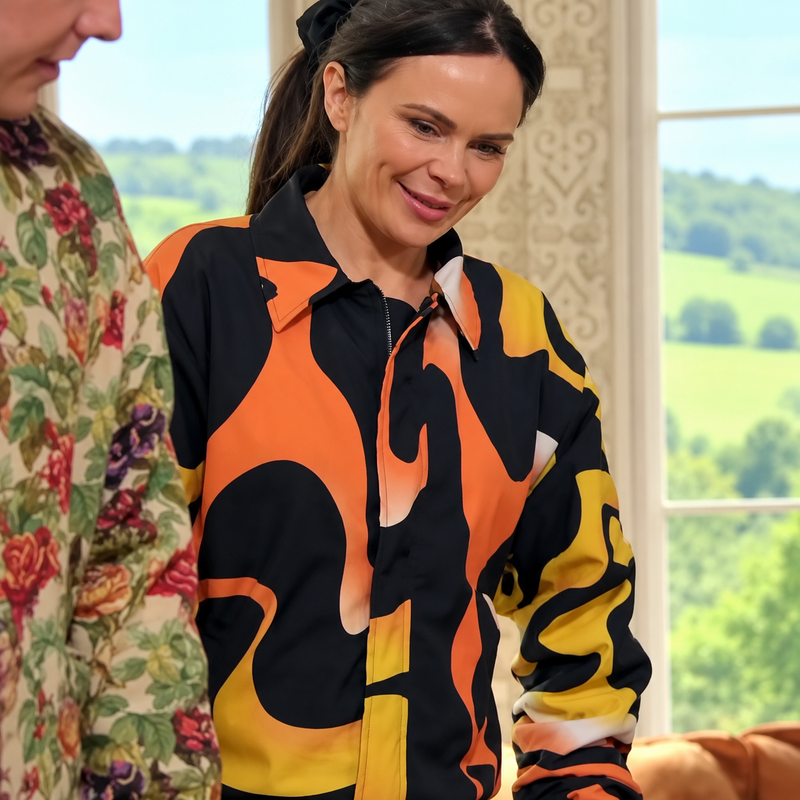 The-Celebrity-Traitors-S02-Oversize-Bomber-Jacket Woman wearing a black, orange, and yellow abstract print bomber jacket inspired by The Celebrity Traitors Season 2.
