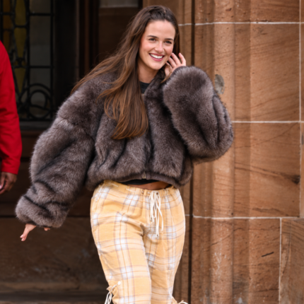 Woman wearing a taupe brown cropped faux fur jacket with oversized sleeves and plush cuffs, styled with yellow plaid trousers outdoors.