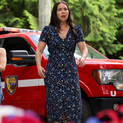 Willow Tait wearing a navy blue floral midi dress with short sleeves and a V-neck in a Fire Country-inspired outdoor setting.