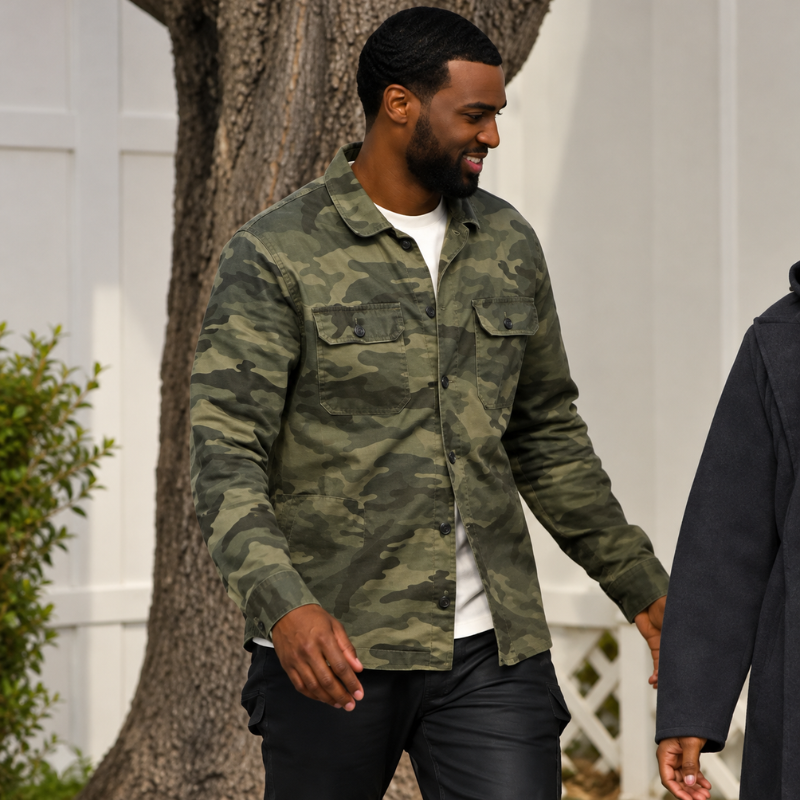 Wilson-monteiro-love-is-blind-season-11-camo-jacket Man wearing a green woodland camouflage shirt jacket over a white T-shirt with black pants in an outdoor setting.