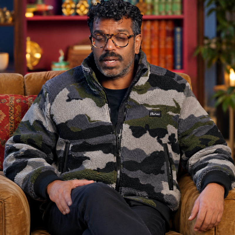 romesh-ranganathan-the-celebrity-traitors-sherpa-fleece-jacket Model wearing a black, gray, and olive green camouflage sherpa fleece jacket with a stand-up collar and front zipper pockets.