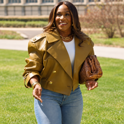 Model wearing a mustard yellow cropped leather belted jacket with gold-tone buttons, a white top, and blue jeans